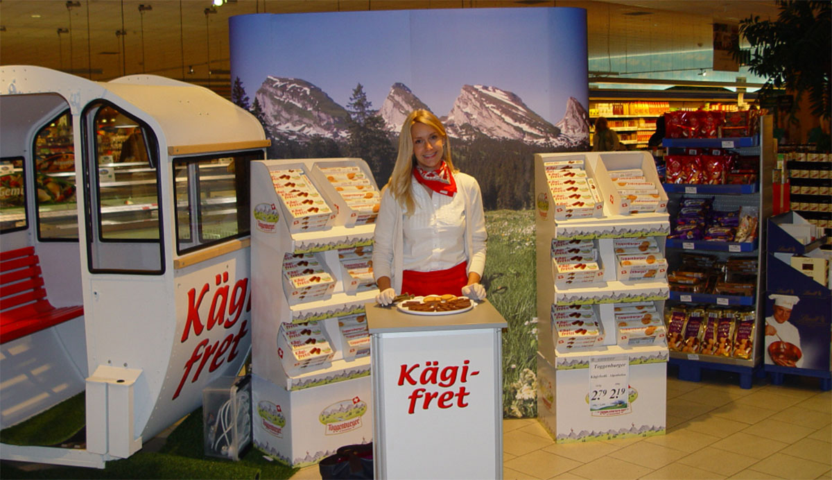 Eine freundliche Frau betreut einen Promotionstand für Kägi fret in einem Supermarkt
