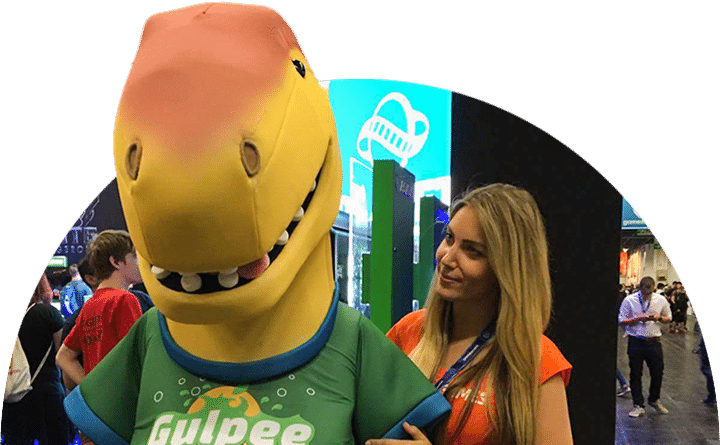 Eine Messehostess steht neben einer Person in einem grinsenden Dinosaurierkostüm